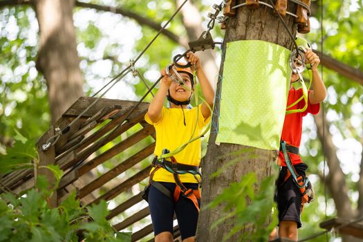 Happy child climbing in the trees. Rope park. Climber child. Early childhood development. Roping park. Balance beam and rope bridges. Rope park - climbing center.