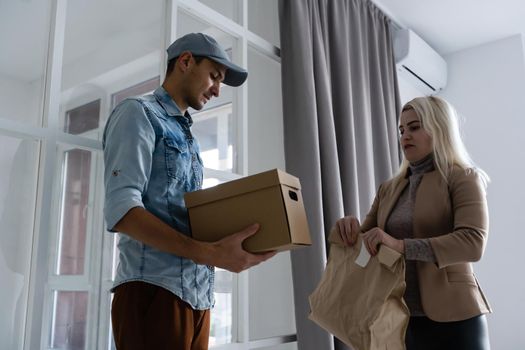 Fast and reliable service. Cheerful young delivery man giving a cardboard box to young woman while standing at the entrance of her apartment.