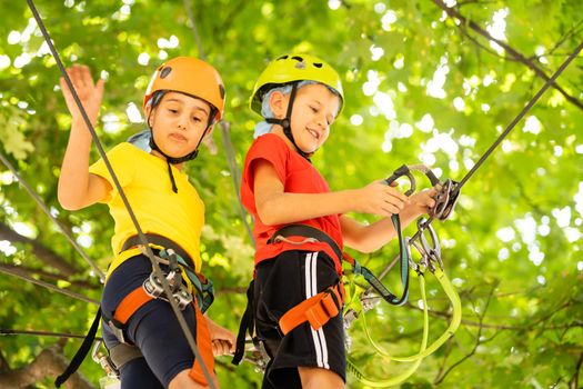 Child in forest adventure park. Kids climb on high rope trail. Agility and climbing outdoor amusement center for children. Little girl playing outdoors. School yard playground with rope way