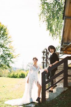 Bride and groom are standing on the steps near the wooden railings of the house. High quality photo