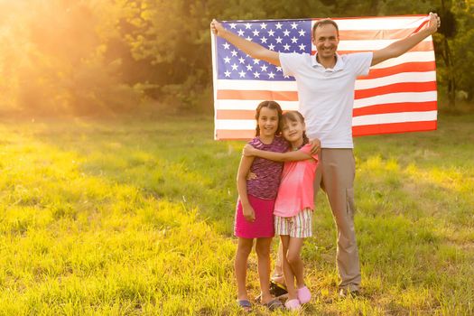 Happy family with the American flag in a wheat field at sunset. Independence Day, 4th of July