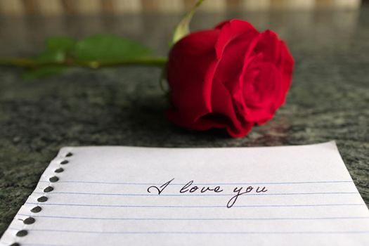 Low angle view of A red Rose on a granite counter with an I Love You Note . High quality photo