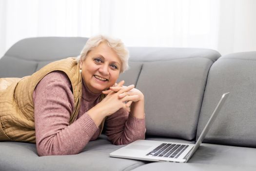 Serious mature older adult woman watching training webinar on laptop working from home or in office. 60s middle aged businesswoman taking notes while using computer technology.