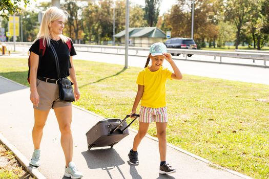 mother and little daughter go with suitcases to the airport. tourism and travel