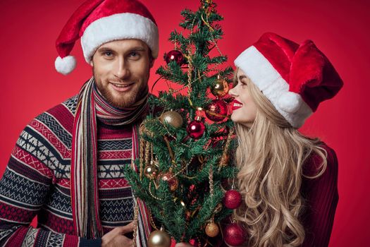 man and woman standing next to christmas tree toys lifestyle red background. High quality photo