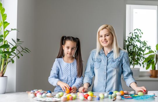 Happy easter. A mother and her daughter painting Easter eggs. Happy family preparing for Easter. Cute little child girl wearing bunny ears on Easter day