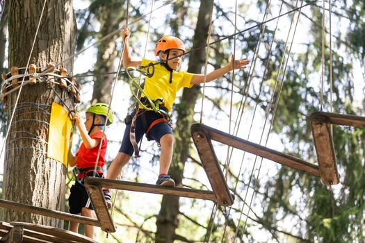 Child in forest adventure park. Kids climb on high rope trail. Agility and climbing outdoor amusement center for children. Little girl playing outdoors. School yard playground with rope way