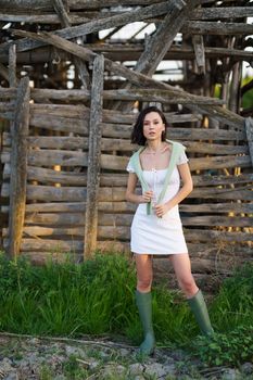 Pretty young Asian woman, posing near a tobacco drying shed, wearing a white dress and green wellies. Beauty and fashion concept