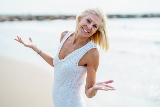 Smiling mature woman opening her arms on a tropical beach. Elderly female enjoying her retirement walking on the beach.