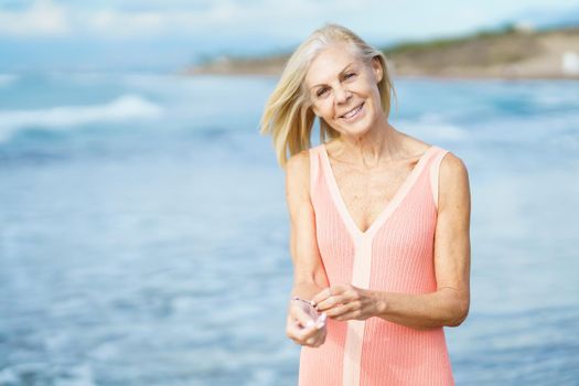 Beautiful mature woman walking along the shore of a tropical beach, wearing a nice orange dress. Elderly female enjoying her retirement at a seaside retreat.