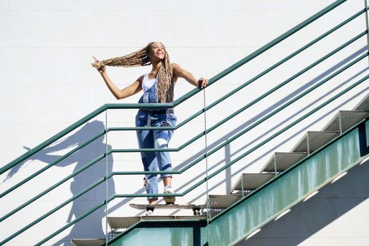 Beautiful young black girl on an urban staircase, holding her coloured braids. Typical African hairstyle.