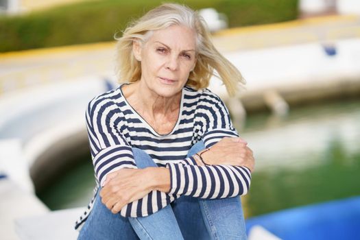 Mature woman looking serenely at the camera, sitting in a seaport.