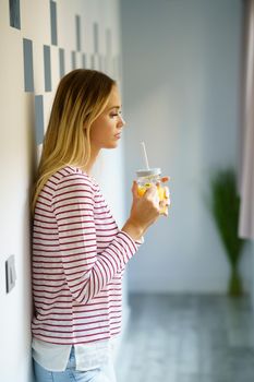 Thoughtful woman drinking a glass of natural orange juice at home.