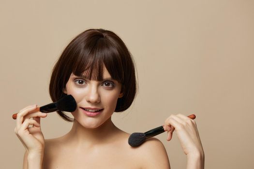 portrait woman makeup brushes near the face bare shoulders isolated background. High quality photo