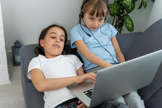 Children receive education at home in a classroom with a laptop, online courses for children, child development, two caucasian girls have fun and watch cartoons, homeshooling.