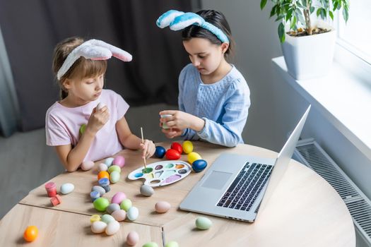 Two little cute girls with bunny ears are painting Easter eggs, children are preparing for the spring holiday, Easter mood, children are drawing on eggs