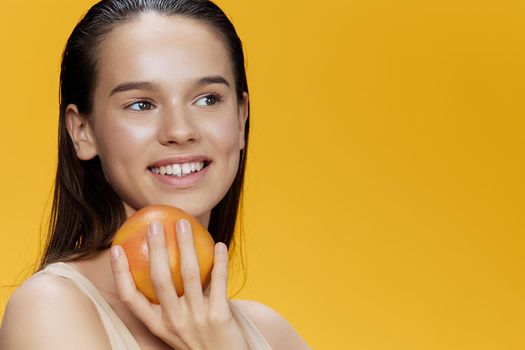 young woman with grapefruit near face clean skin care health yellow background. High quality photo