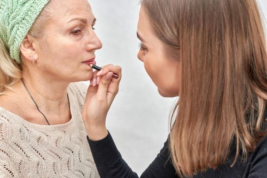 Woman at the reception at the beautician applies makeup. The master brings the lips with a cosmetic pencil