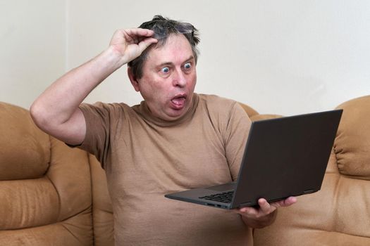 A man at the age of sitting on Devani looks through the news on a laptop. The man stuck out his tongue in surprise