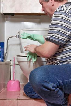 A man puts on household rubber gloves to wash a dirty toilet.