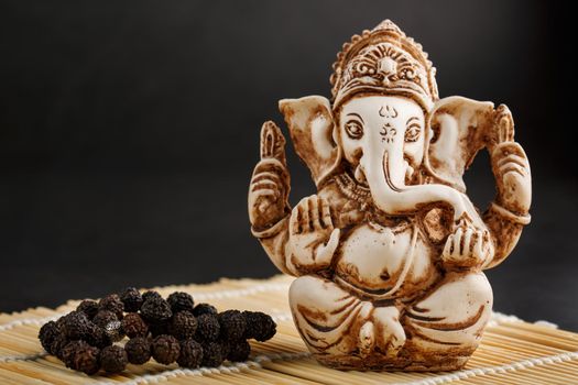 Hindu god Ganesh on a black background. Rudraksha statue and rosary on a wooden table with a red incense stick and incense smoke. Copy space