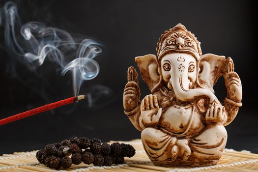 Ganesha on a black background. Statue and rosary with red smoldering incense stick Ganesha sahasranama