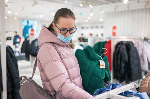 Woman wearing protective face mask shopping clothes in retail shopping store. Concept of lifestyle during corona virus pandemic.