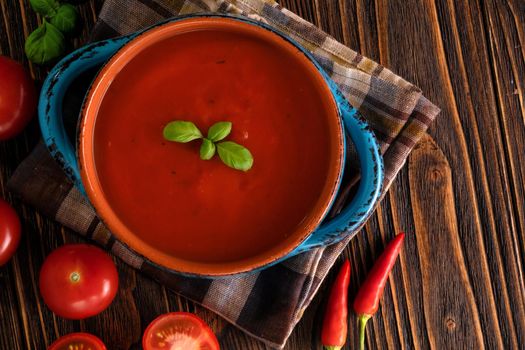 Traditional tomato cream soup and food ingredients on wooden table.
