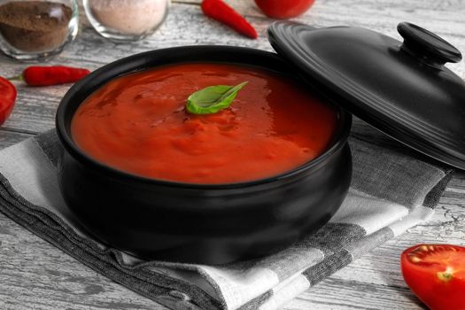 Traditional tomato cream soup and food ingredients on wooden table.