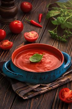 Traditional tomato cream soup and food ingredients on wooden table.