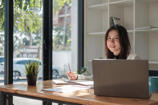 Charming Asian woman with a smile working for financial marketing plan using laptop computer.