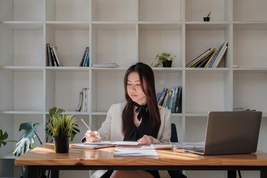 Portrait of young businesswoman working with laptop computer while taking note on notepad at her office.