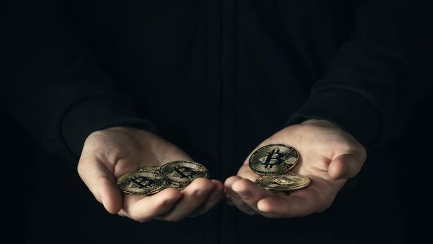 Handful of bitcoins in male palmson a dark background. Financial savings, accumulation in cryptocurrency concept. Selective focus.