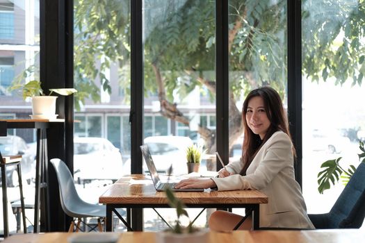 Side view young asian businesswoman sitting on her workplace in the office. Young woman working for financial document data charts with laptop in the office