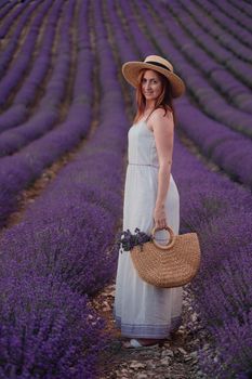 charming Young woman with a hat and white dress in a purple lavender field. LIfestyle outdoors. Back view.