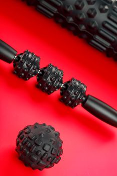 Set of Black lumpy foam massage roller, body roller, rubber ball on red background. For the mechanical and reflex effects on tissues and organs.