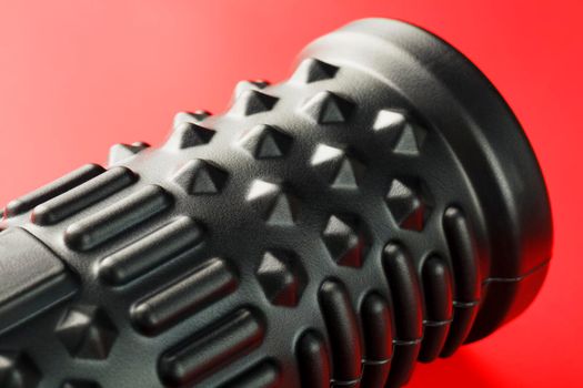 Black lumpy foam massage roller on red background. For the mechanical and reflex effects on tissues and organs. Close-up, texture, element in macro