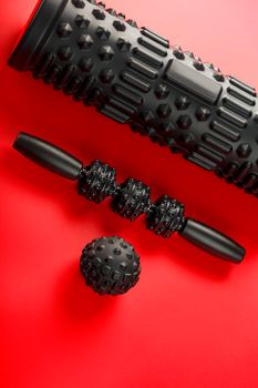 Set of Black lumpy foam massage roller, body roller, rubber ball on red background. For the mechanical and reflex effects on tissues and organs.