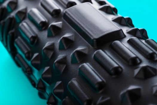 Black bumpy foam massage roller, body roller on blue background. For the mechanical and reflex effects on tissues and organs.