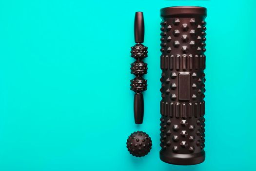 A set of black bumpy foam massage rollers, body rollers, rubber balls on a blue background for mechanical and reflex action on tissues and organs.