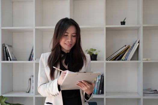 Portrait of business asian woman happy smile holding check list on clipboard and pen at modern offlice.