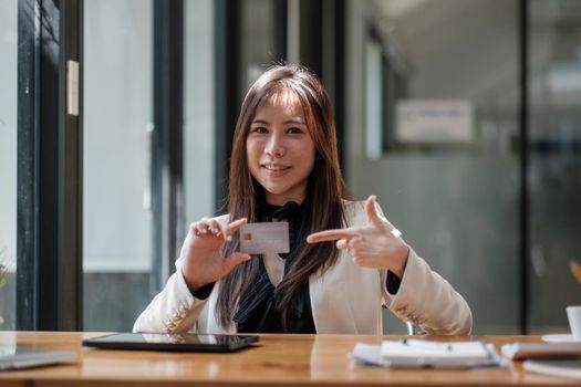 Smiling charming asian woman showing credit card on hand, online shopping and payment concept.