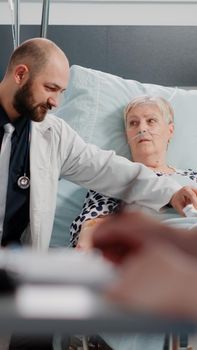 Doctor talking to retired woman with disease in hospital ward bed for healthcare consultation. Medic doing medical checkup for sick patient with nasal oxygen tube and IV drip bag.