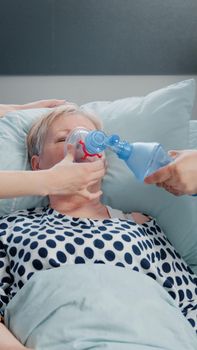 Doctor and nurse using oxygen tube for hyperventilating woman in bed. Medical specialists with tool and heart rate monitor for reanimation and respiratory problem of senior patient.