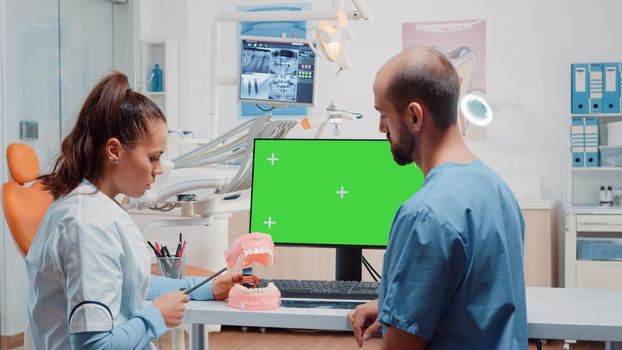 Nurse and dentist examining teeth layout using green screen on computer. Dentistry specialists looking at chroma key and isolated background on monitor for oral and dentition care