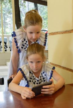 Two twin caucasian girls 9 years are looking at the smartphone