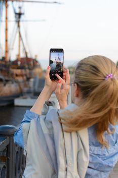 Woman takes pictures of yacht by phone. Sunset, rear view. Selective focus