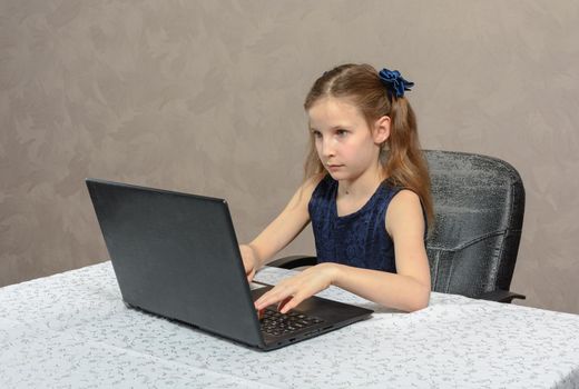 Teen schoolgirl 9 years old of european appearance does her homework on laptop