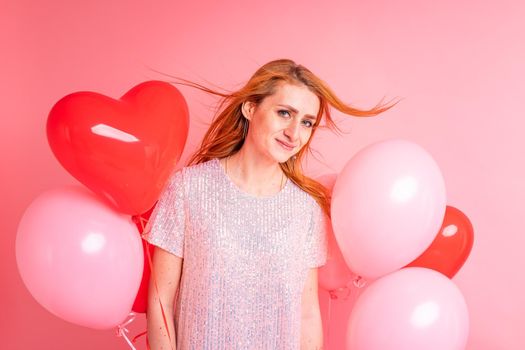 Beautiful redhead girl with red heart baloon posing. Happy Valentine's Day concept. Studio photo of beautiful ginger girl dancing on pink background.