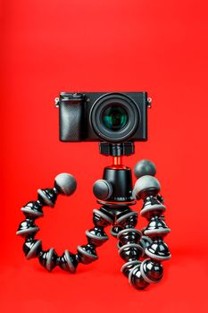 Professional camera on a tripod, on a red background. Record videos and photos for your blog, reportage. Free space, isolated.